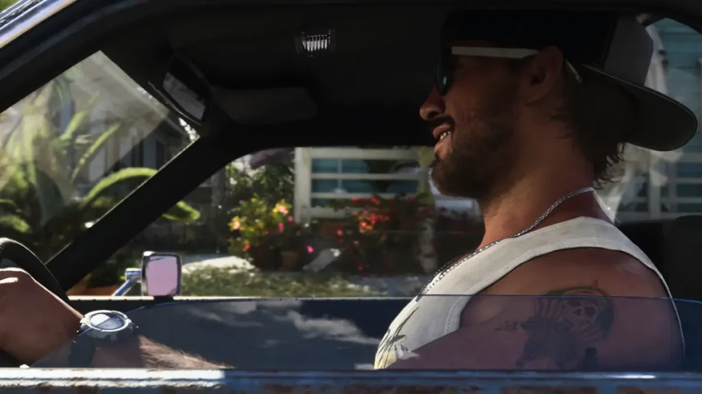 Jason smiling while driving a car in GTA 6 Trailer 2, showcasing detailed character design and lush background scenery.