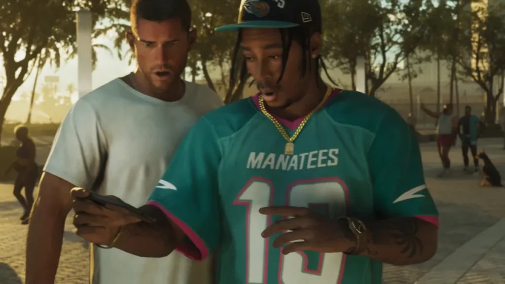 Two GTA 6 characters react to a phone screen, one wearing a teal Manatees jersey, in a sunny urban park
